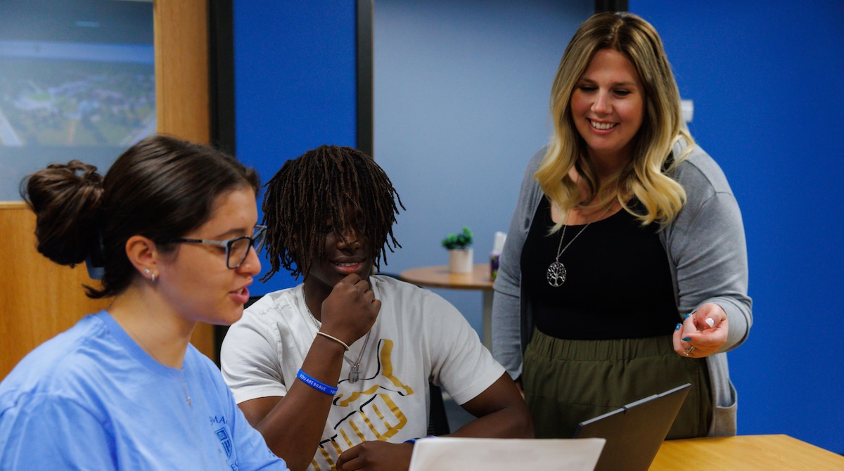 Two students and one instructor collaborate around a laptop in a bright office setting.