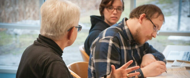 Female instructor talking to two students at a table.