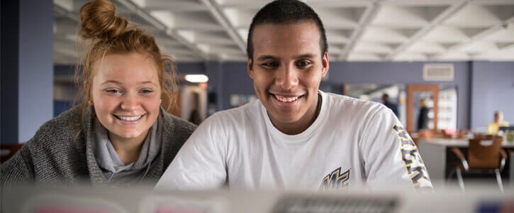 Two students looking at a laptop smiling.