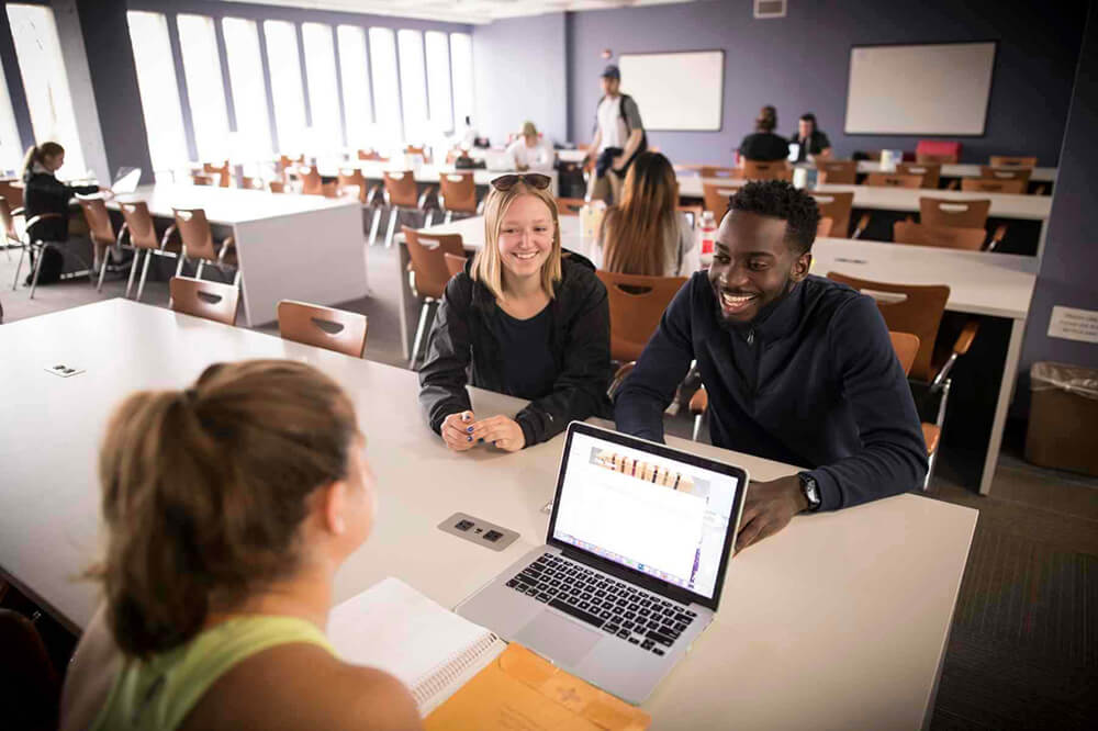 Three students sitting in a classroom working on a project together.