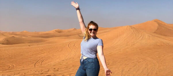 Merrimack student standing in a desert holding one hand up over her head, wearing sunglasses and ...