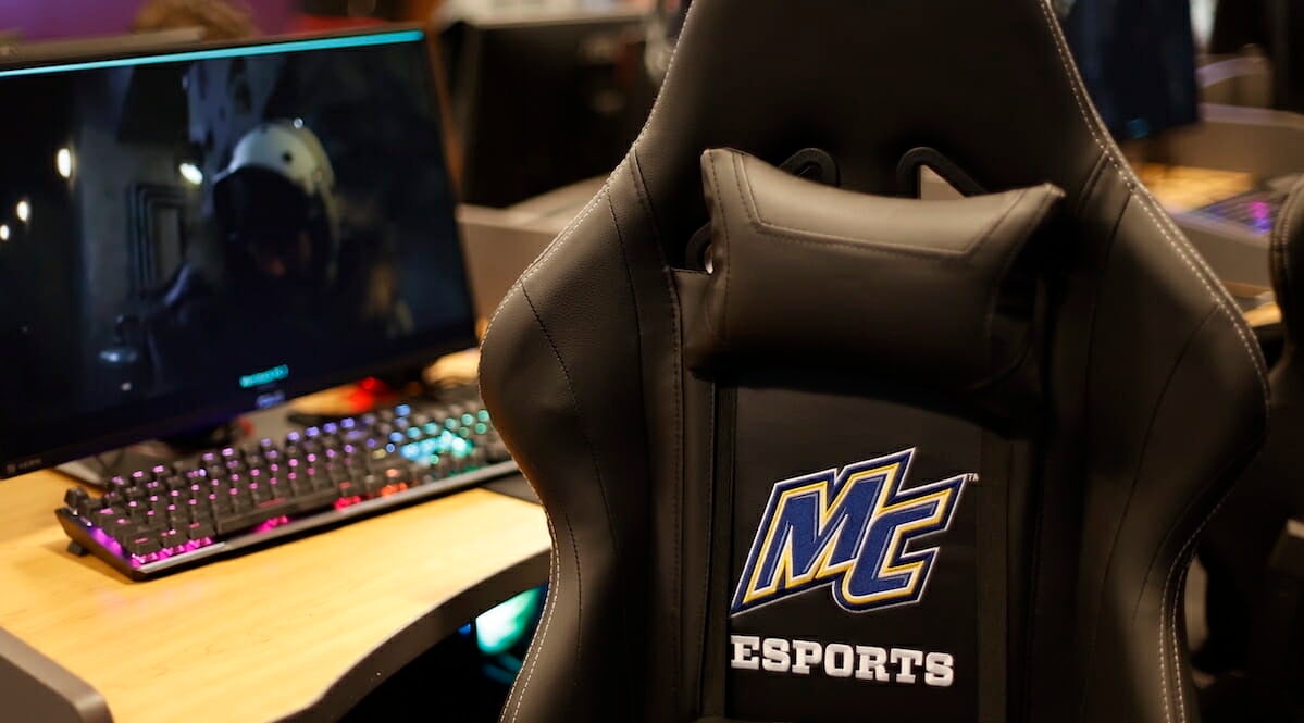 A computer and gaming chair with an embroidered Merrimack College Esports logo