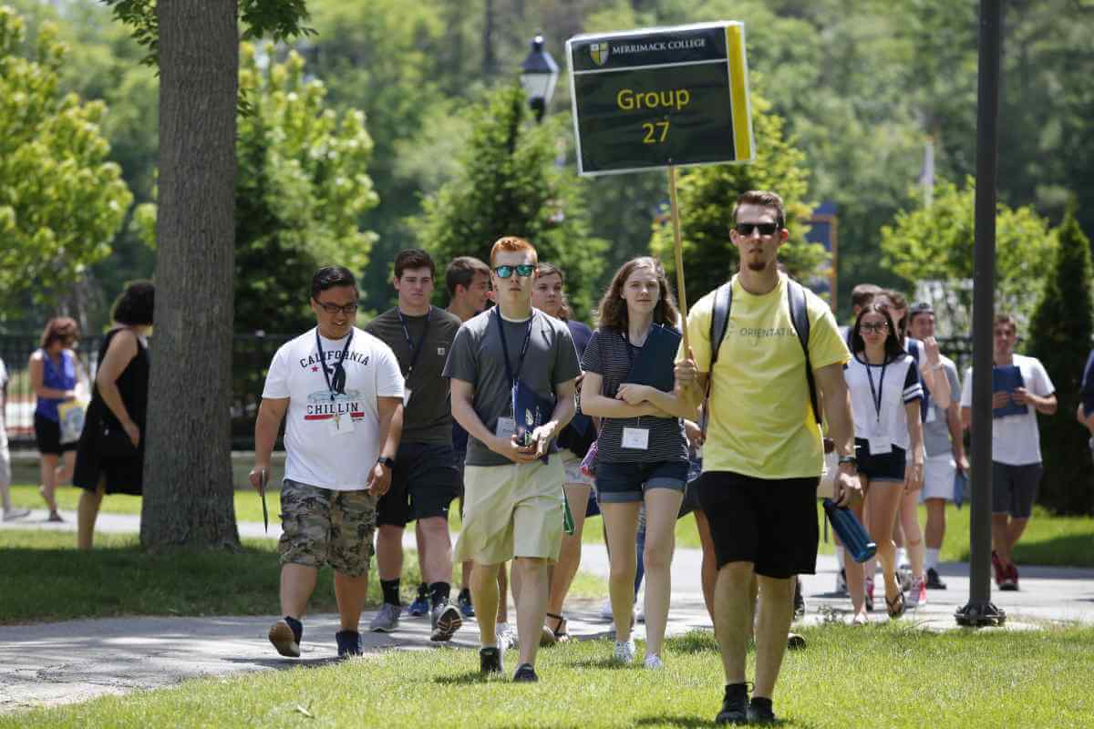 Orientation Leader holding a sign leading students across the grass.