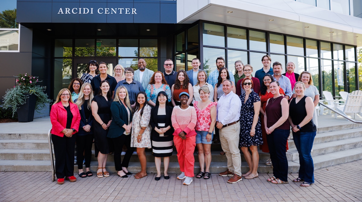 A group of people smiling and posing together outside the Arcidi Center building entrance.