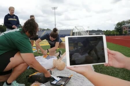 Athletic trainers on field with medical manikin.