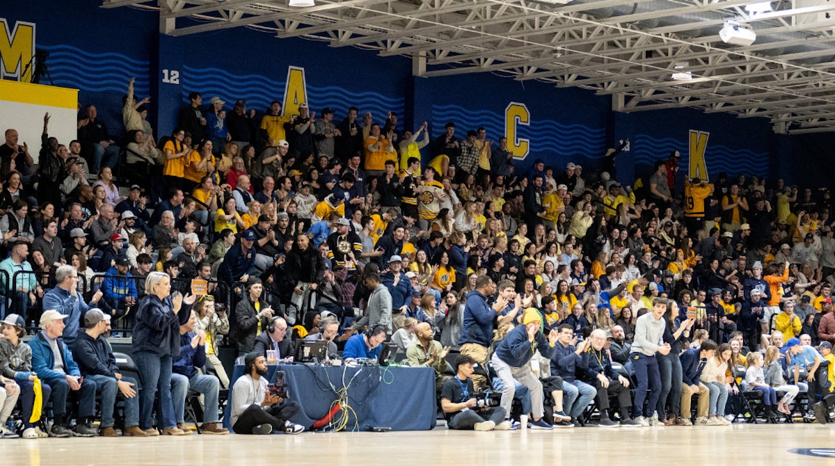 Photo of a crowd of spectators in the stands watching Merrimack men's basketball.