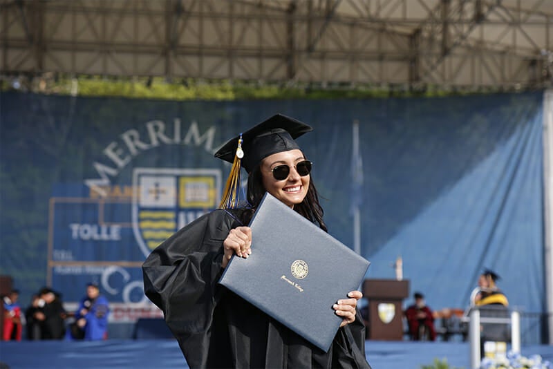 Student holding up diploma in front of Commencement stage