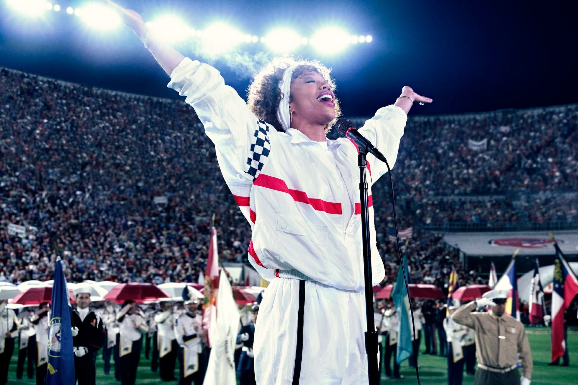 Still from the film, "I Wanna Dance With Somebody," showing actress Naomi Ackie as Whitney Houston singing the National Anthem at the 1991 Super Bowl.