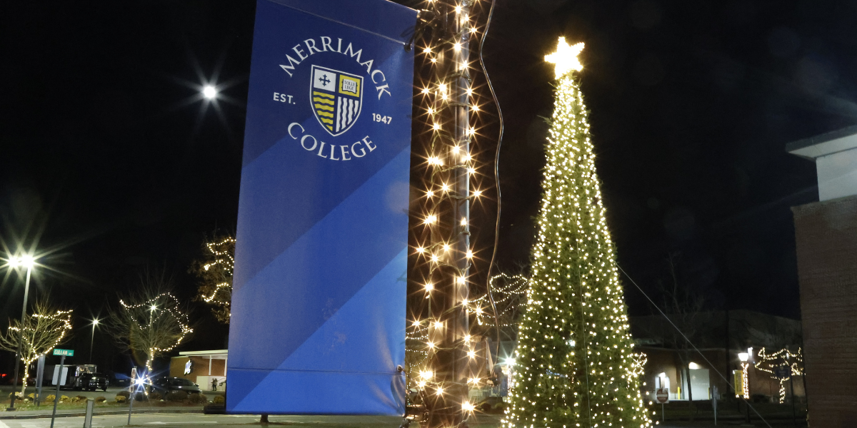 Photo of a Christmas tree next to a Merrimack College banner.