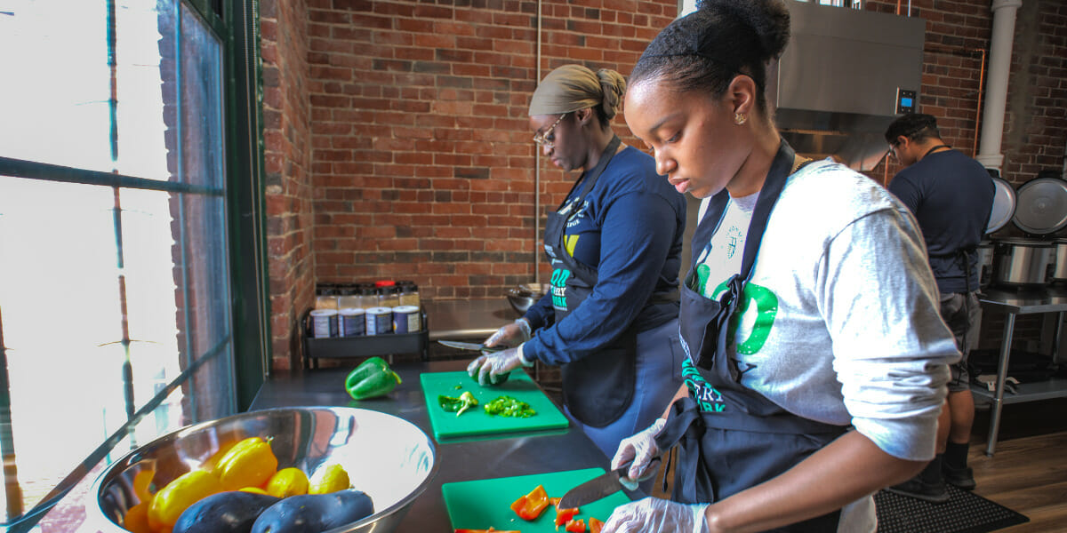 Two student volunteers chop vegetables in Hands to Help's new meal prep kitchen