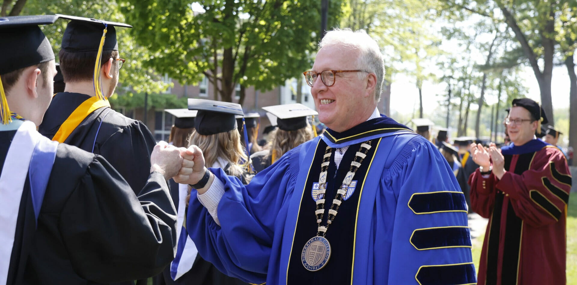 President Hopey fist bumps student dressed in regalia