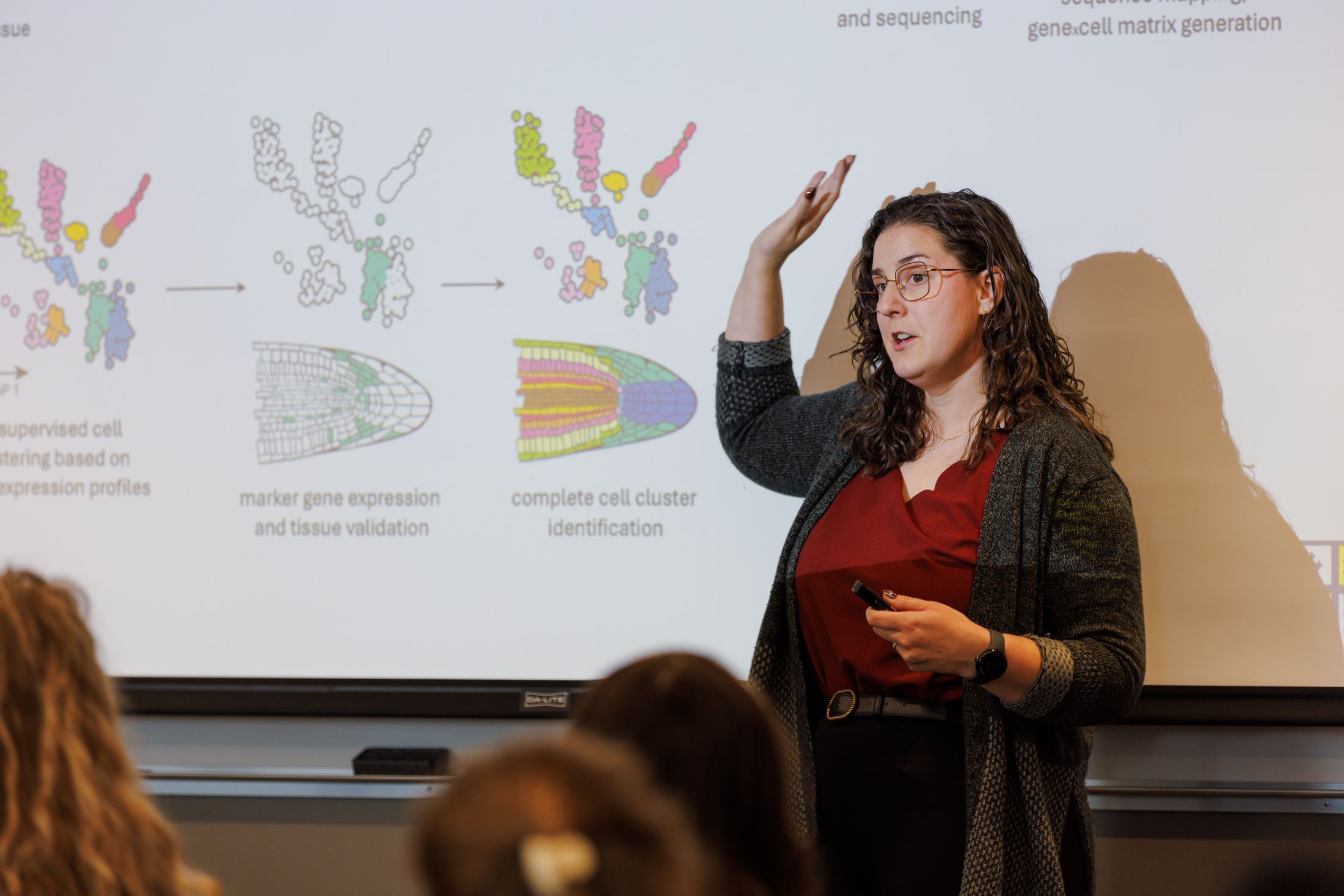 Professor with hand raised as she presents cells on the board