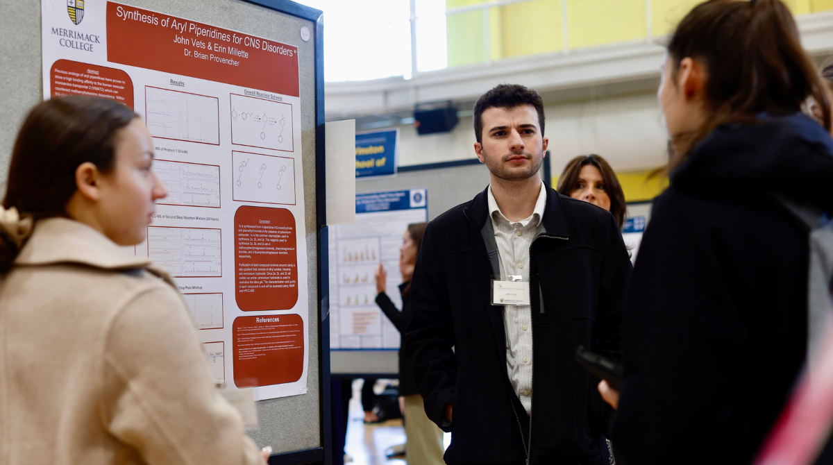 Photo of a student showcasing a poster outlining their senior research project to two people.