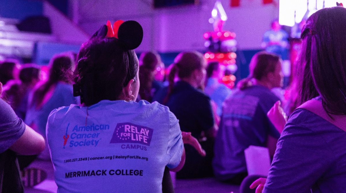 Student wearing a ‘Relay for Life’ shirt at this year's event, surrounded by a crowd in purple lighting