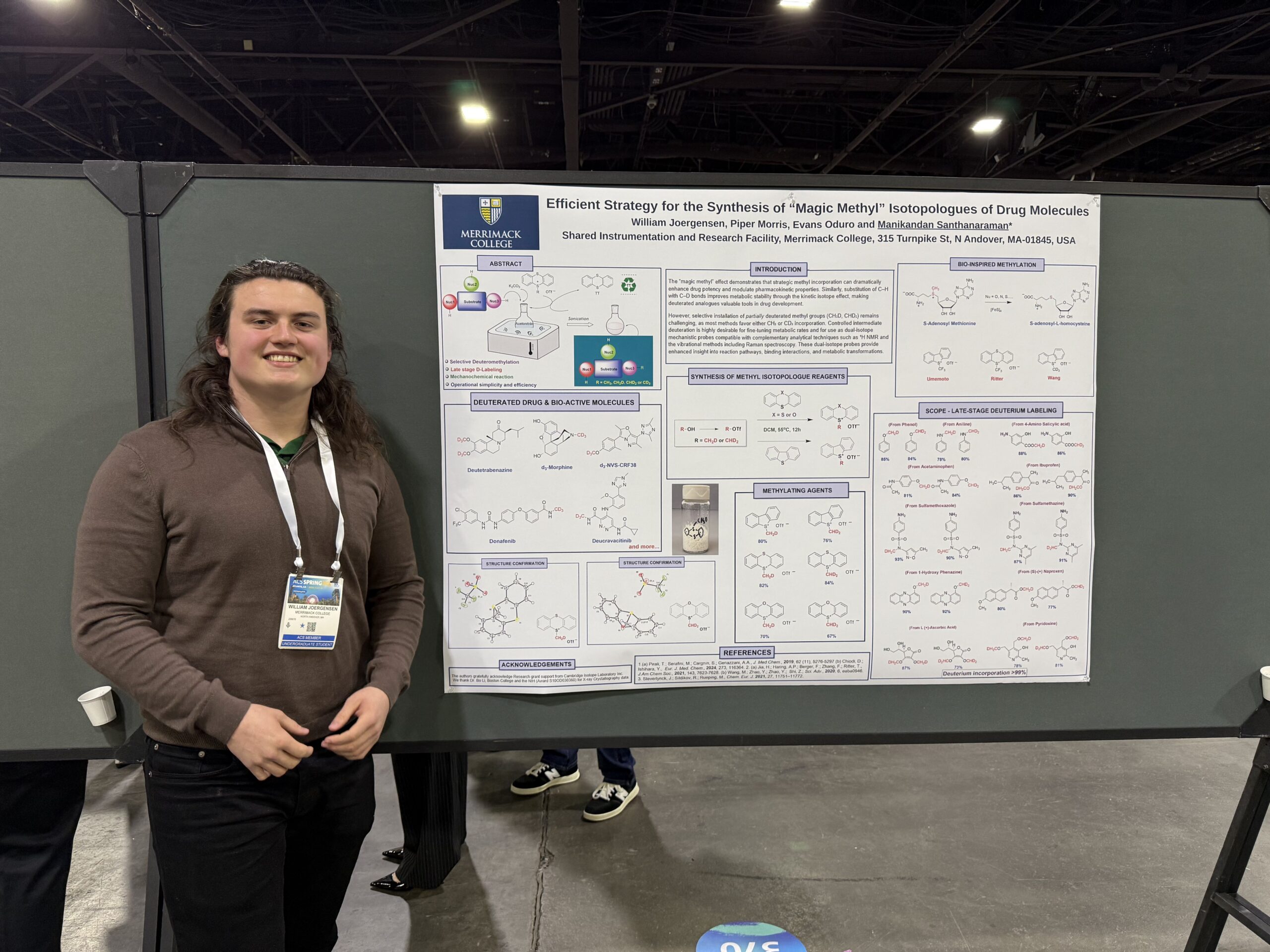 Student William Joergensen standing in front of his academic poster presentation, entitled "Efficient Strategy for the Synthesis of ‘Magic Methyl’ Isotopologues of Drug Molecules"