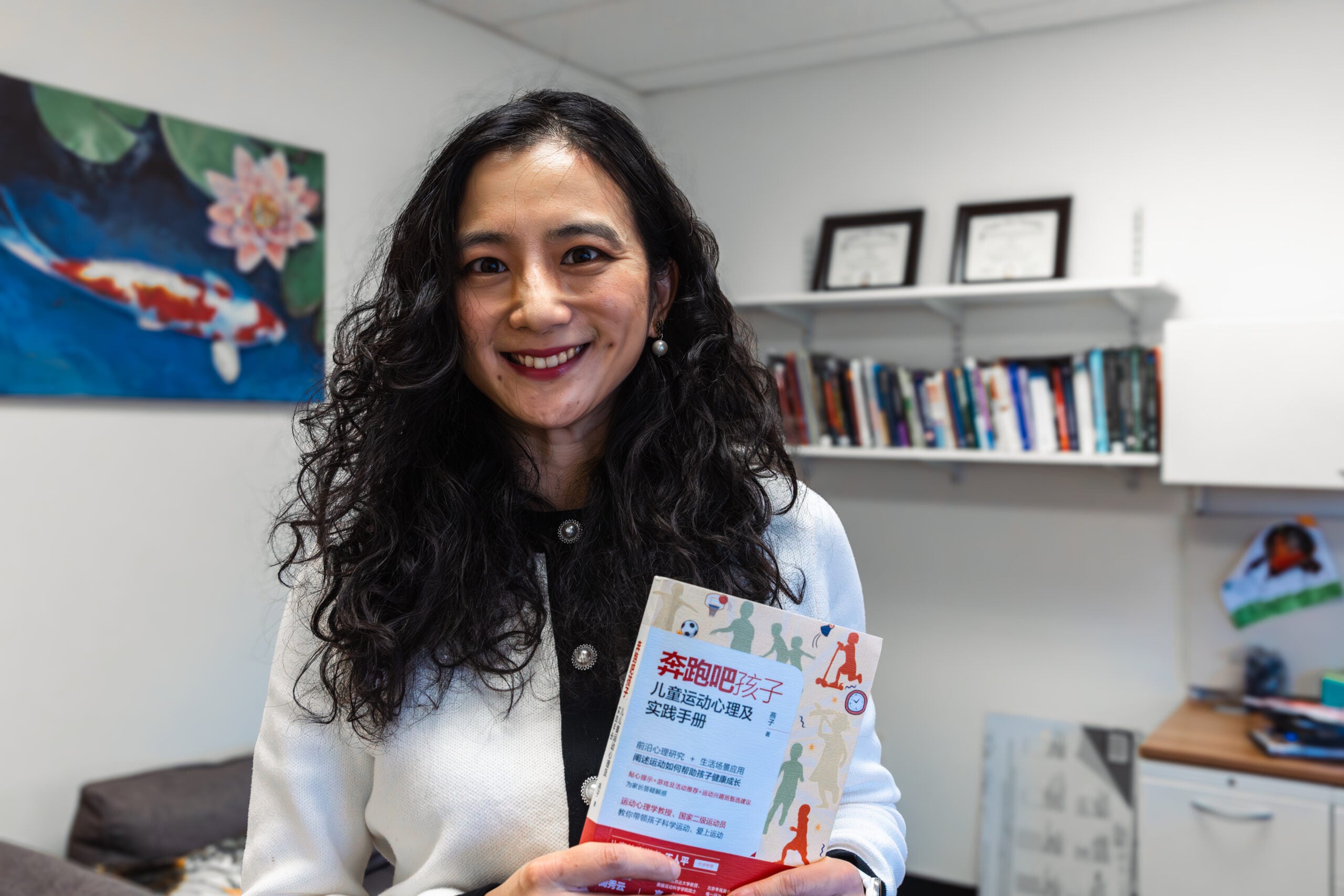 Photo of Zi Yan holding a copy of her book, “Run Kids: Exercise Physiology and Parents Practice Guide,”