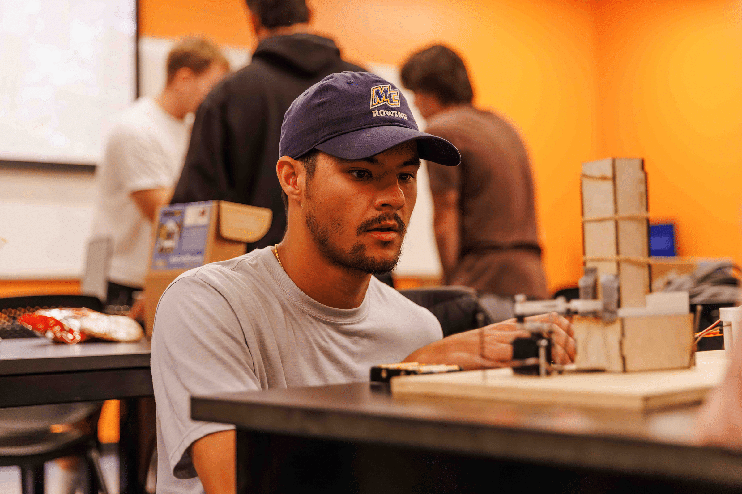 Student works on a small architectural model at a table in a classroom.
