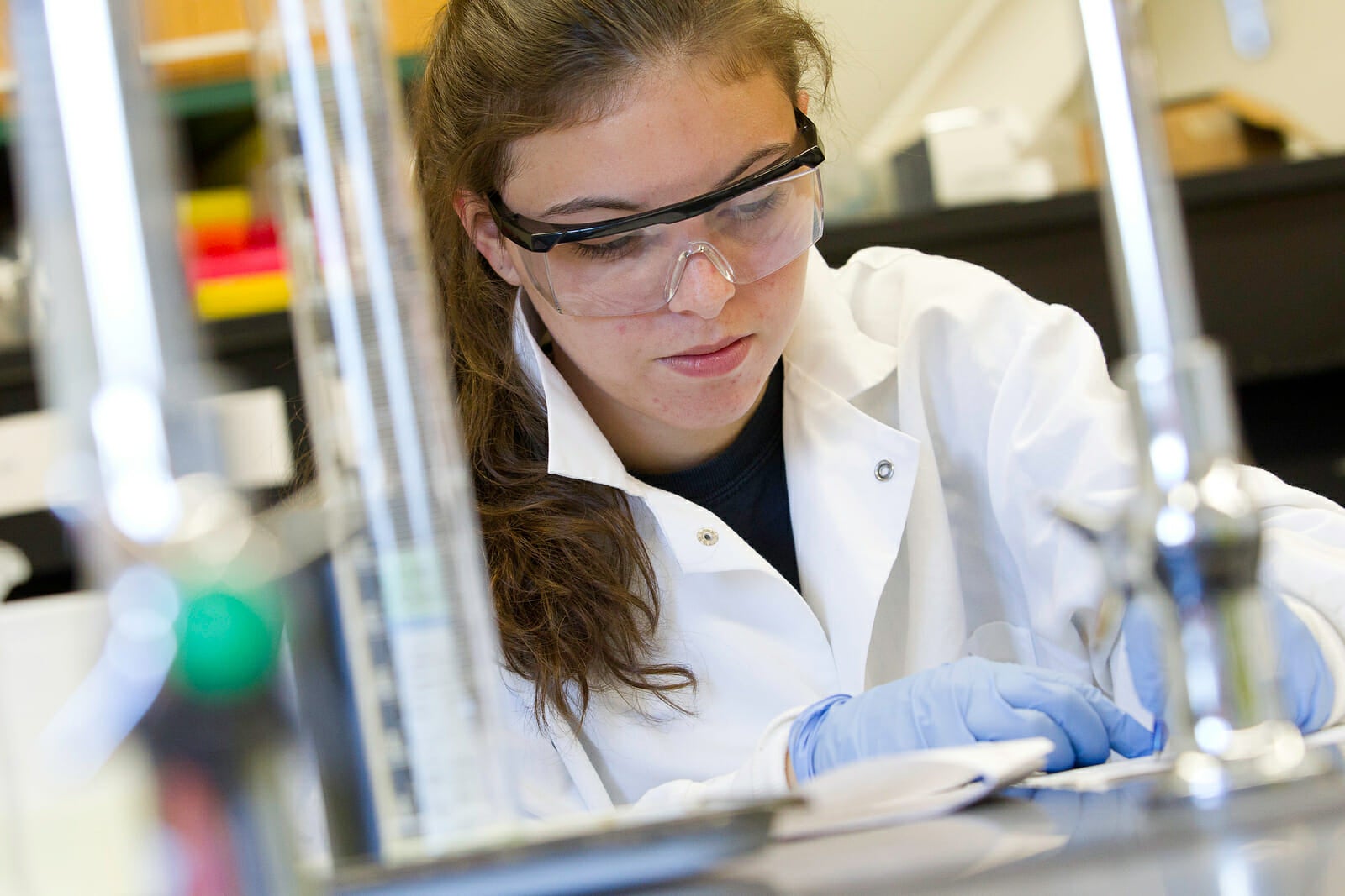 Student wearing lab glasses and lab coat working on task in lab