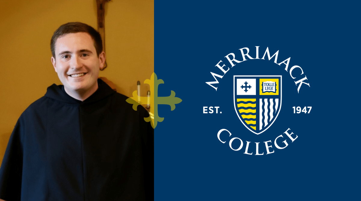 A smiling young man in a black clerical robe standing in a church in front of an altar and crucifix.