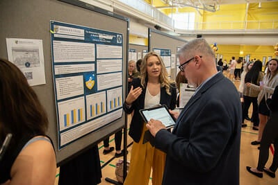 A Merrimack College student discusses her research to an attendee at Merrimack's Research Creative and Achievement Conference.