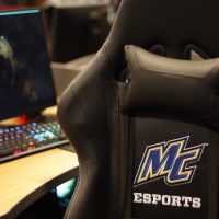 A computer and gaming chair with an embroidered Merrimack College Esports logo