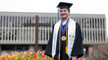 Photo of Maxwell Beland '24 standing outside McQuade Library in his graduation regalia.