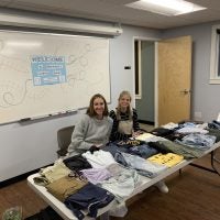 Brooklyn Stolgitis and Jessica McGee sit behind piles of donated clothes.