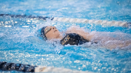 Swimmer wearing goggles performs backstroke in a pool during a competitive swim meet.