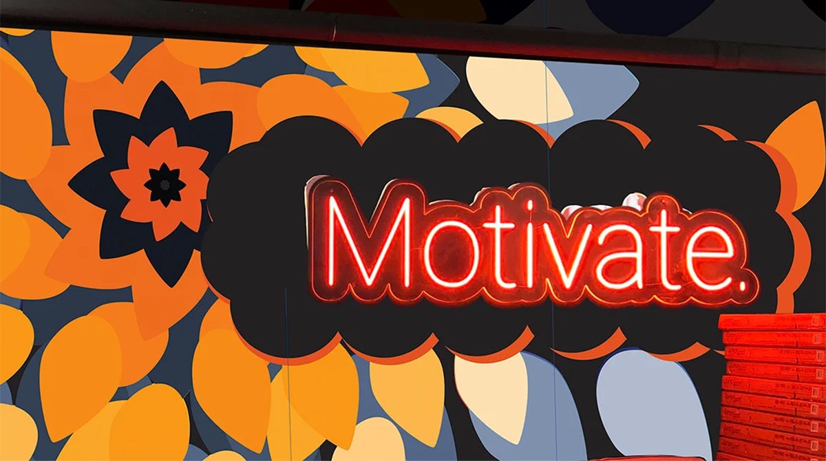 Letters spelling out "Motivate" in neon sign sitting in front of orange and blue abstract art pattern
