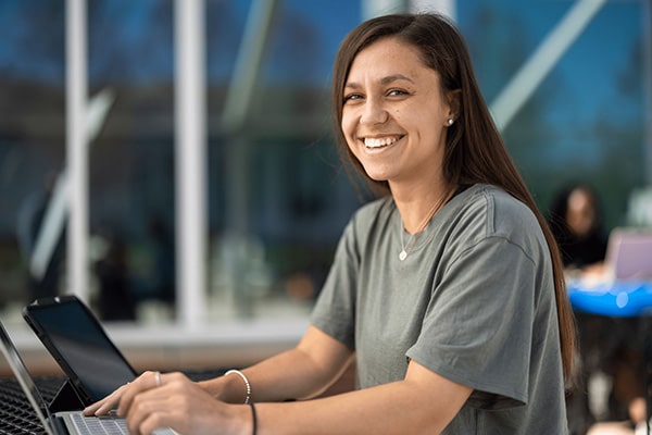 Female student smiling at camera while working on laptop