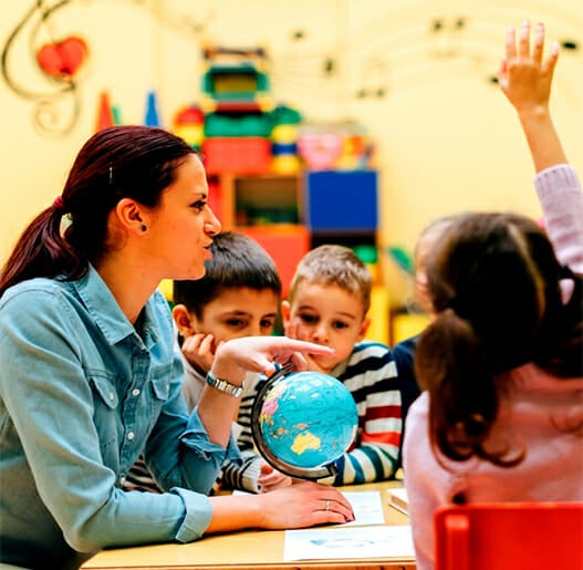 Child raising hand as teacher talks to table of children